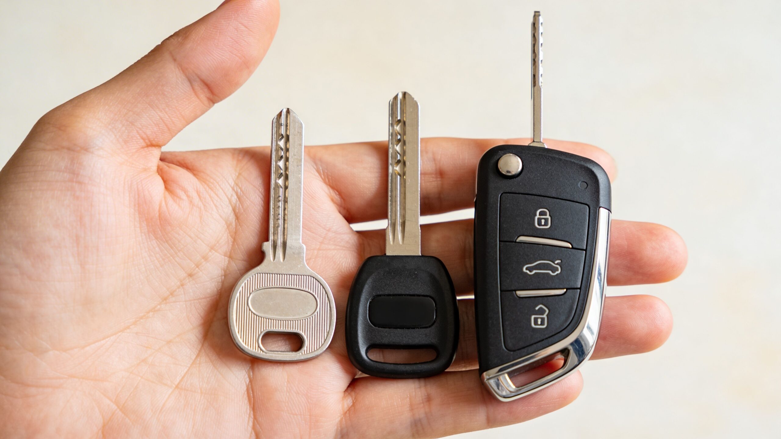 A hand holds three different styles of car keys, including a basic metal key and a remote fob.