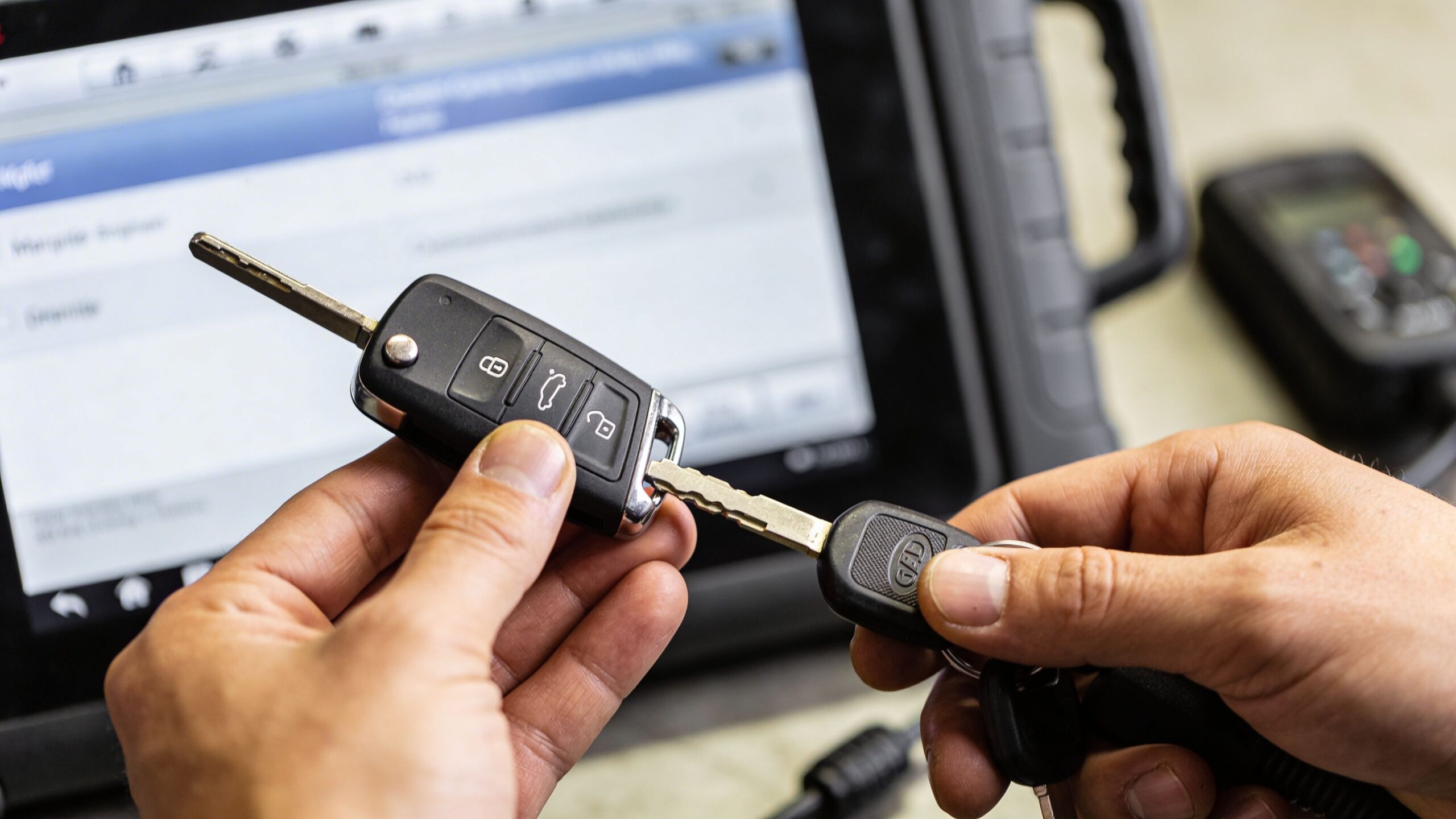 A technician holds a car key fob while using a diagnostic tablet for vehicle key programming.